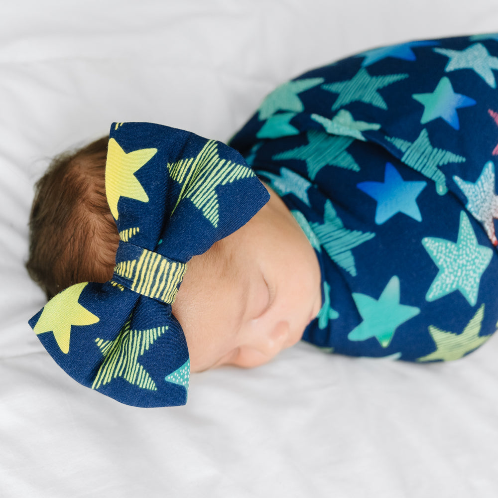Click to see full screen - Close up image of a child swaddled in a Shades of Stars swaddle & luxe bow headband set