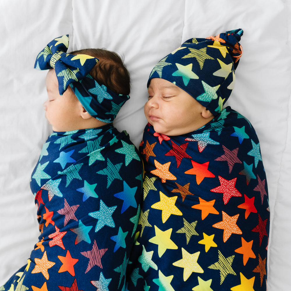 Click to see full screen - Two children together swaddled in matching Shades of Stars swaddle & luxe bow headband and hat set