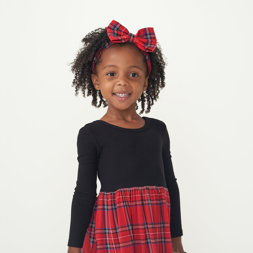 Close up image of a child wearing a Holiday Plaid skater dress and matching luxe bow headband