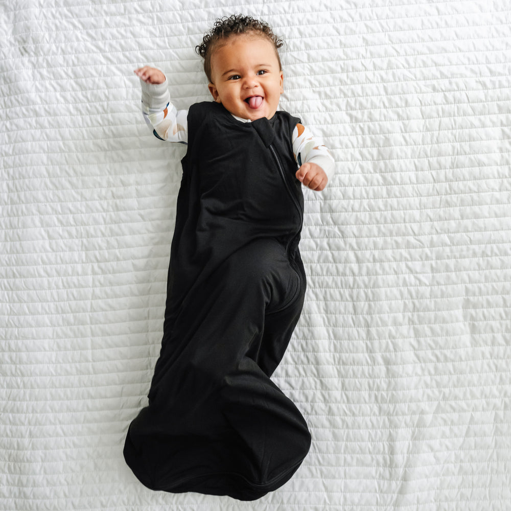 Click to see full screen - Alternate image of a child laying on a blanket wearing a Black sleepy bag and coordinating zippy