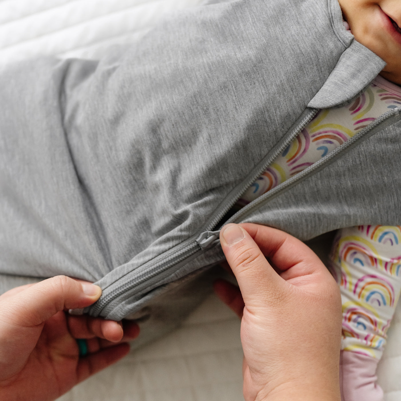 Close up image of a parent zipping up a Heather Gray Sleepy Bag