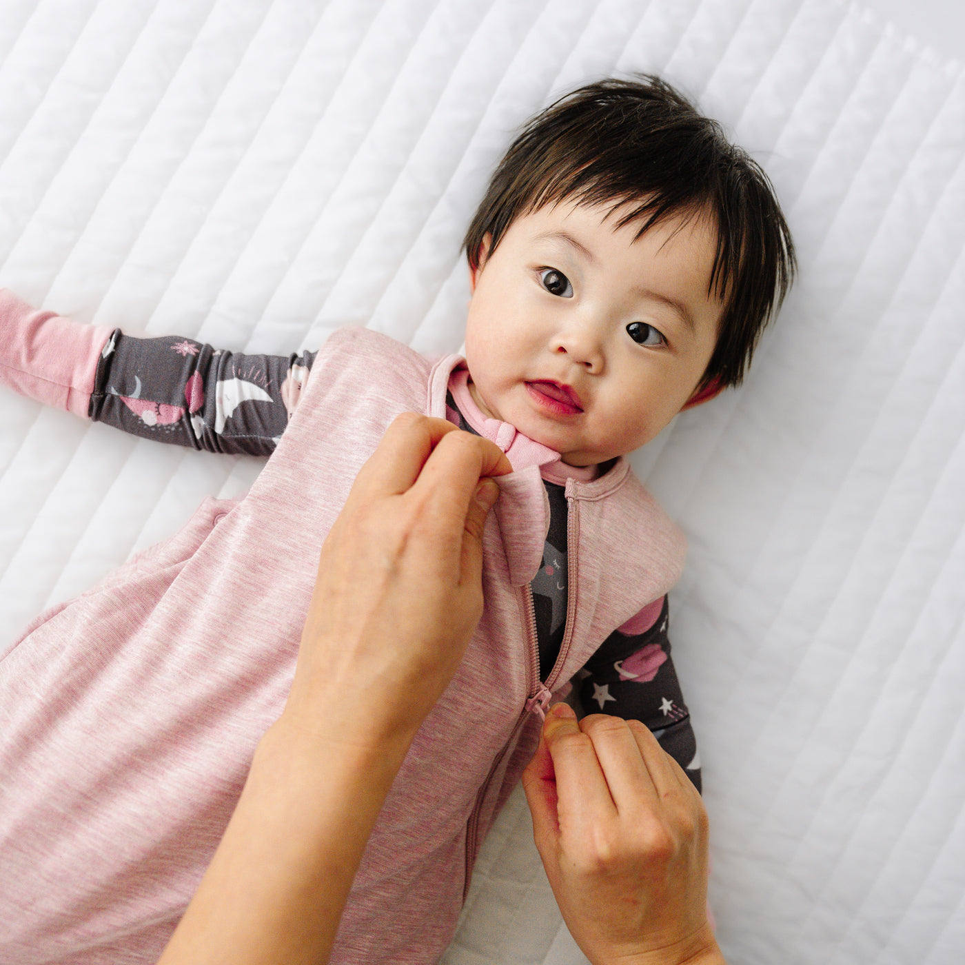 Child laying on a blanket while a parent zips up the Heather Mauve sleepy bag they are wearing
