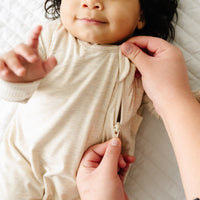 Close up image of a child wearing a Heather Oatmeal sleepy bag while a parent zips it up