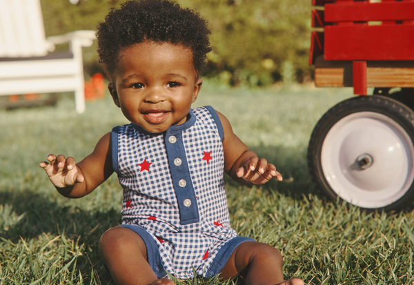 Child wearing a blue and white checkered outfit with red stars, sitting on grass.