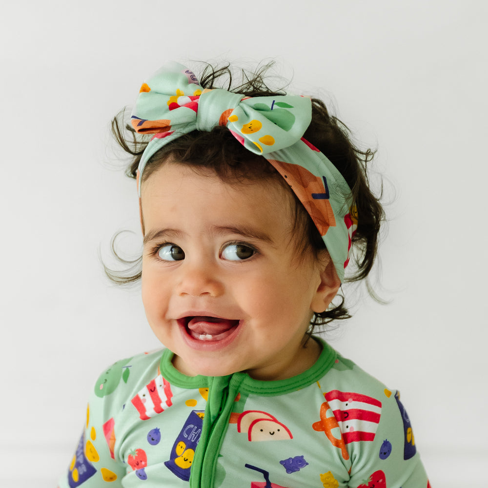 Child posing wearing a Snack Attack printed luxe bow headband paired with a matching zippy