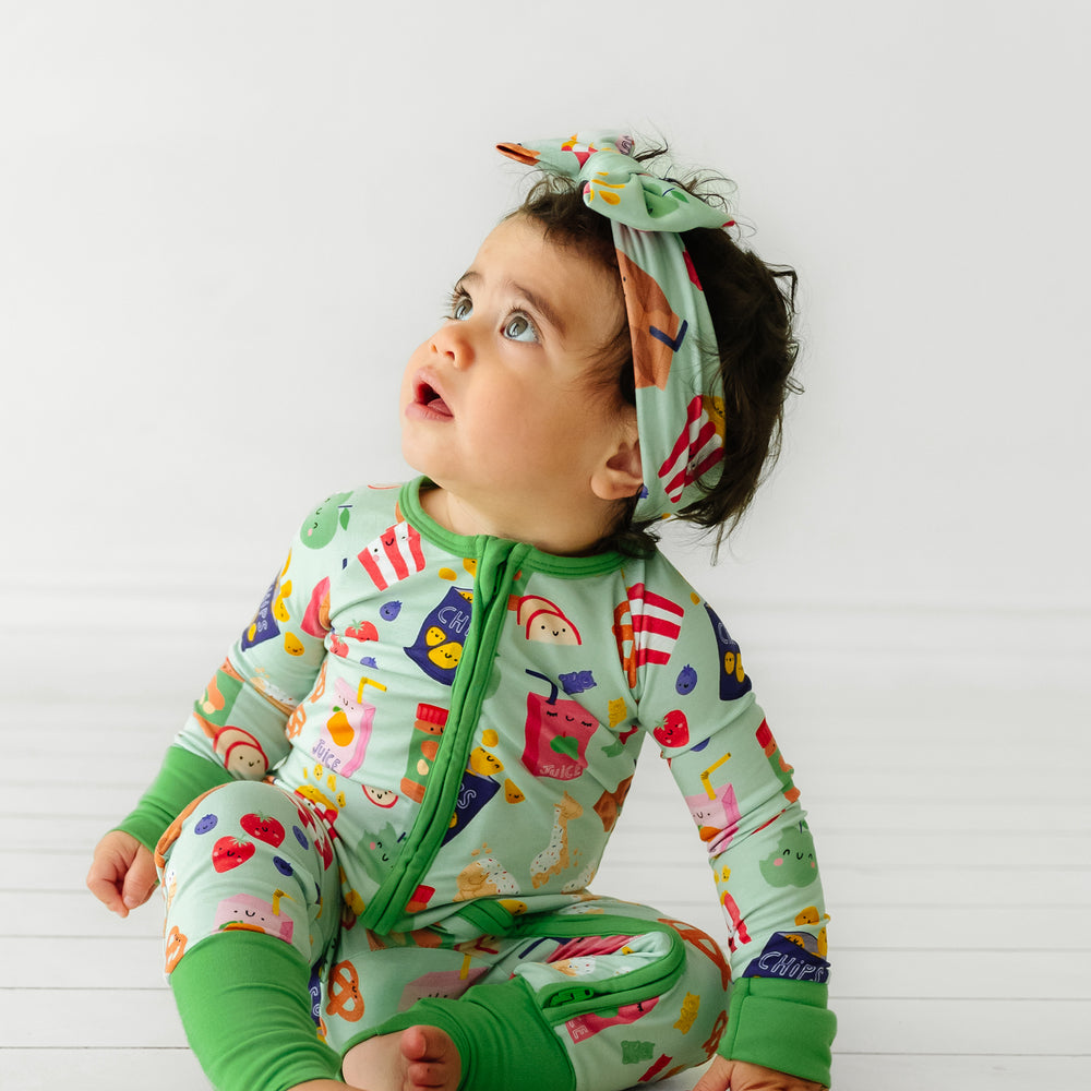 Alternate image of a child sitting wearing a Snack Attack printed luxe bow headband paired with a matching zippy