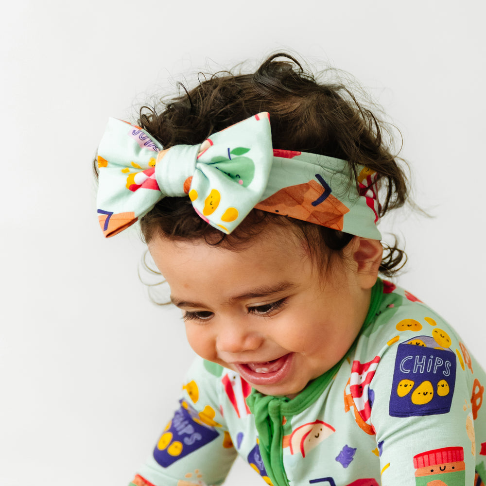 Close up image of a child wearing a Snack Attack luxe bow headband paired with a matching zippy