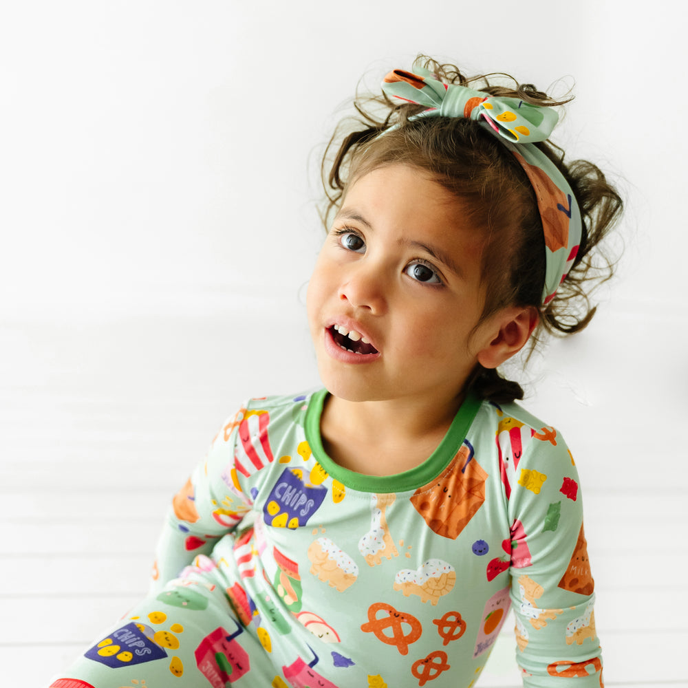Child wearing a Snack Attack printed luxe bow headband paired with a matching two piece pajama set