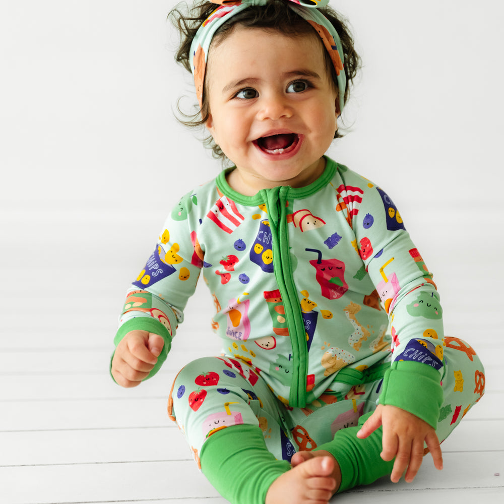 Child sitting wearing a Snack Attack zippy paired with a Snack Attack luxe bow headband