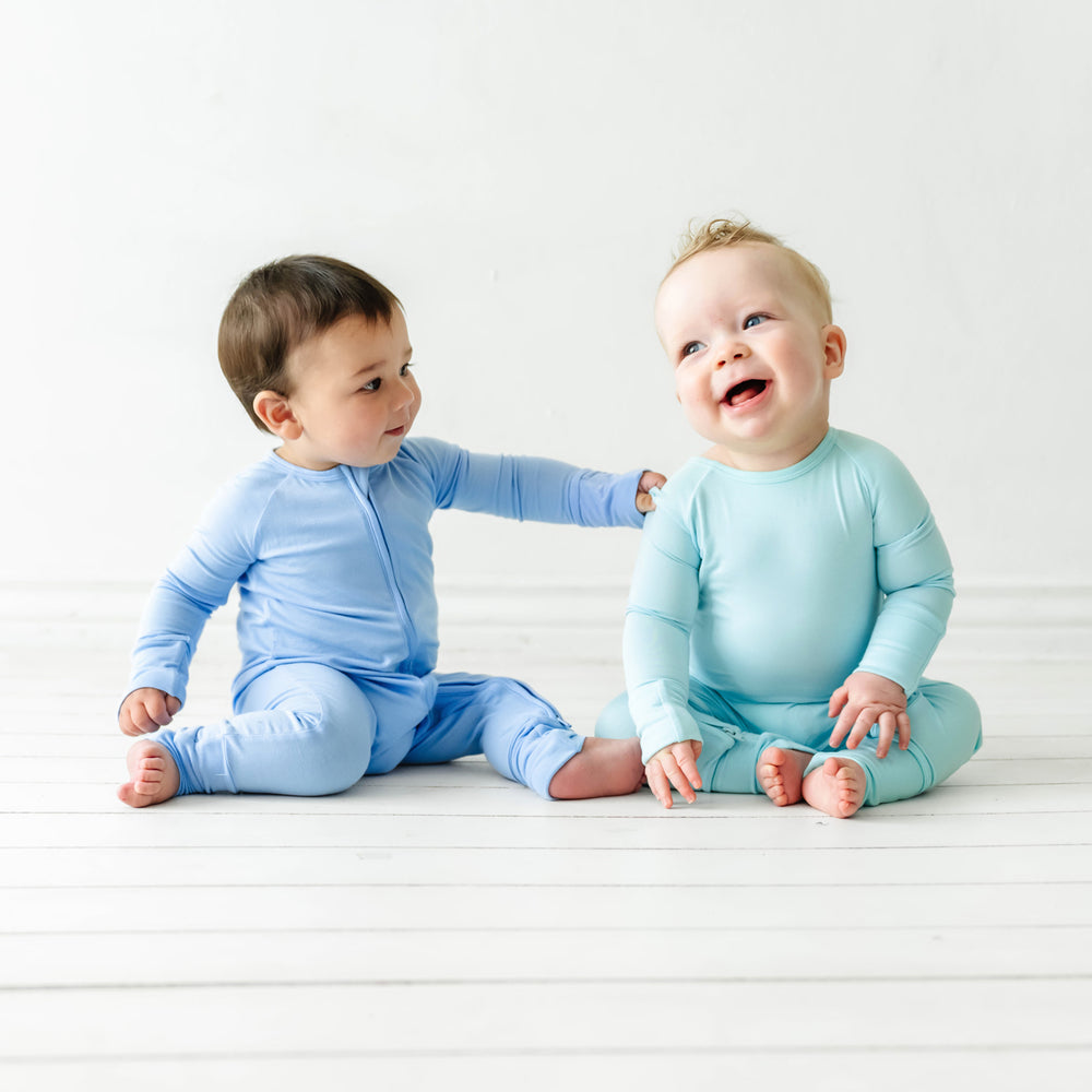 Click to see full screen - Two children sitting together playing. One child is wearing an Aquamarine crescent zippy and one child is wearing a Periwinkle Blue zippy