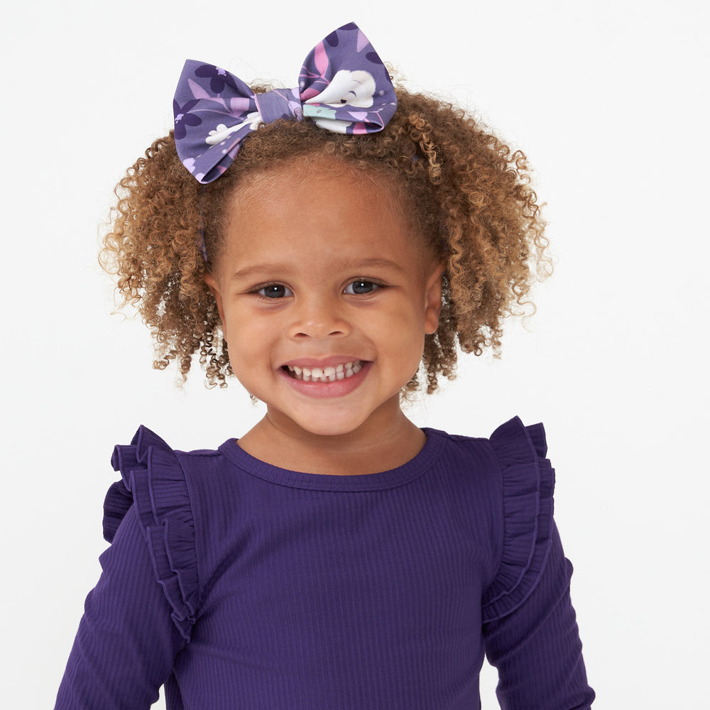 Close up image of a child wearing a Sugar Plum Floral luxe bow headband paired with a Deep Amethyst cozy lettuce tee