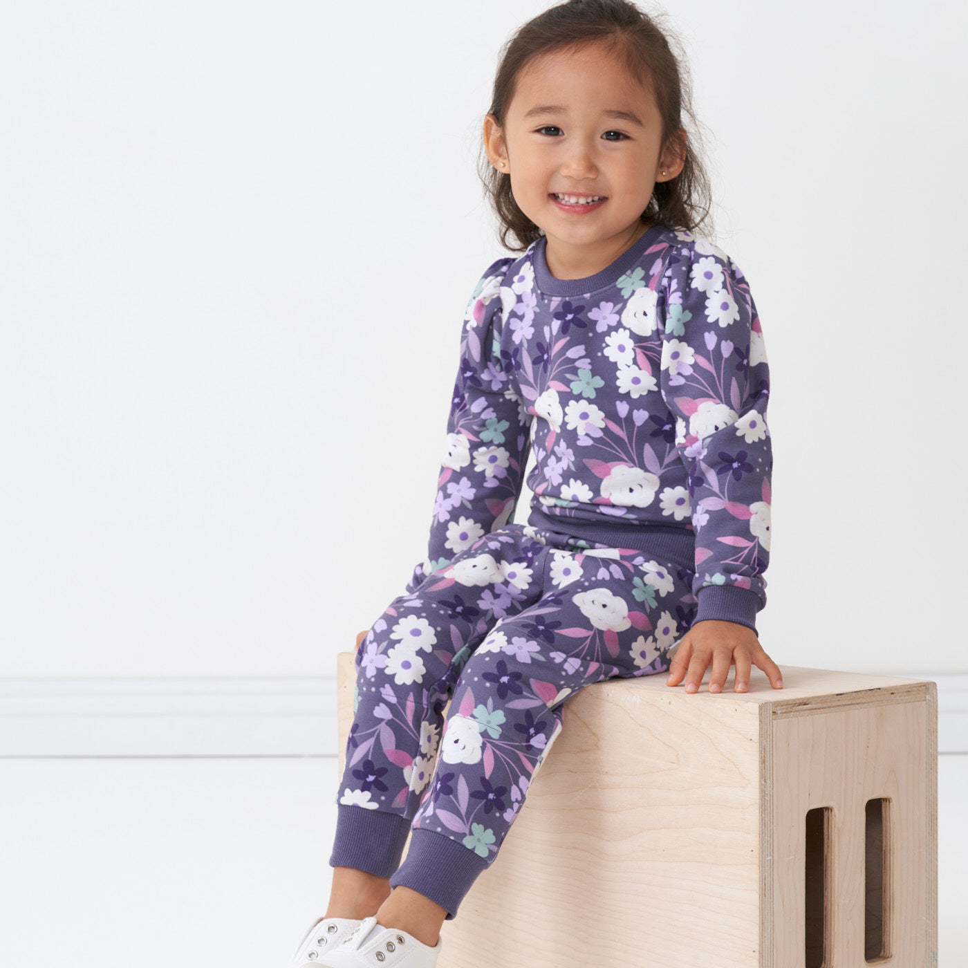 Child sitting on a bench wearing a Sugar Plum Floral puff sleeve crewneck paired with matching joggers