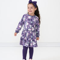 Child wearing a Sugar Plum floral drop waist dress paired with a Deep Amethyst luxe bow headband and Cozy Lettuce leggings 