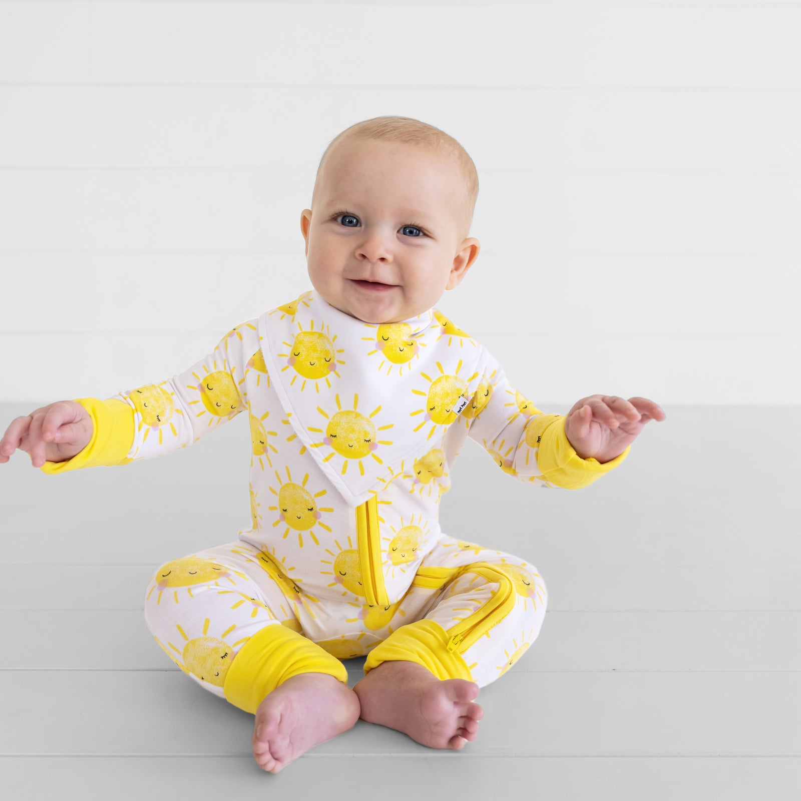 Child sitting on the ground wearing a Sunshine Bandana Bib over matching Sunshine bamboo pajamas