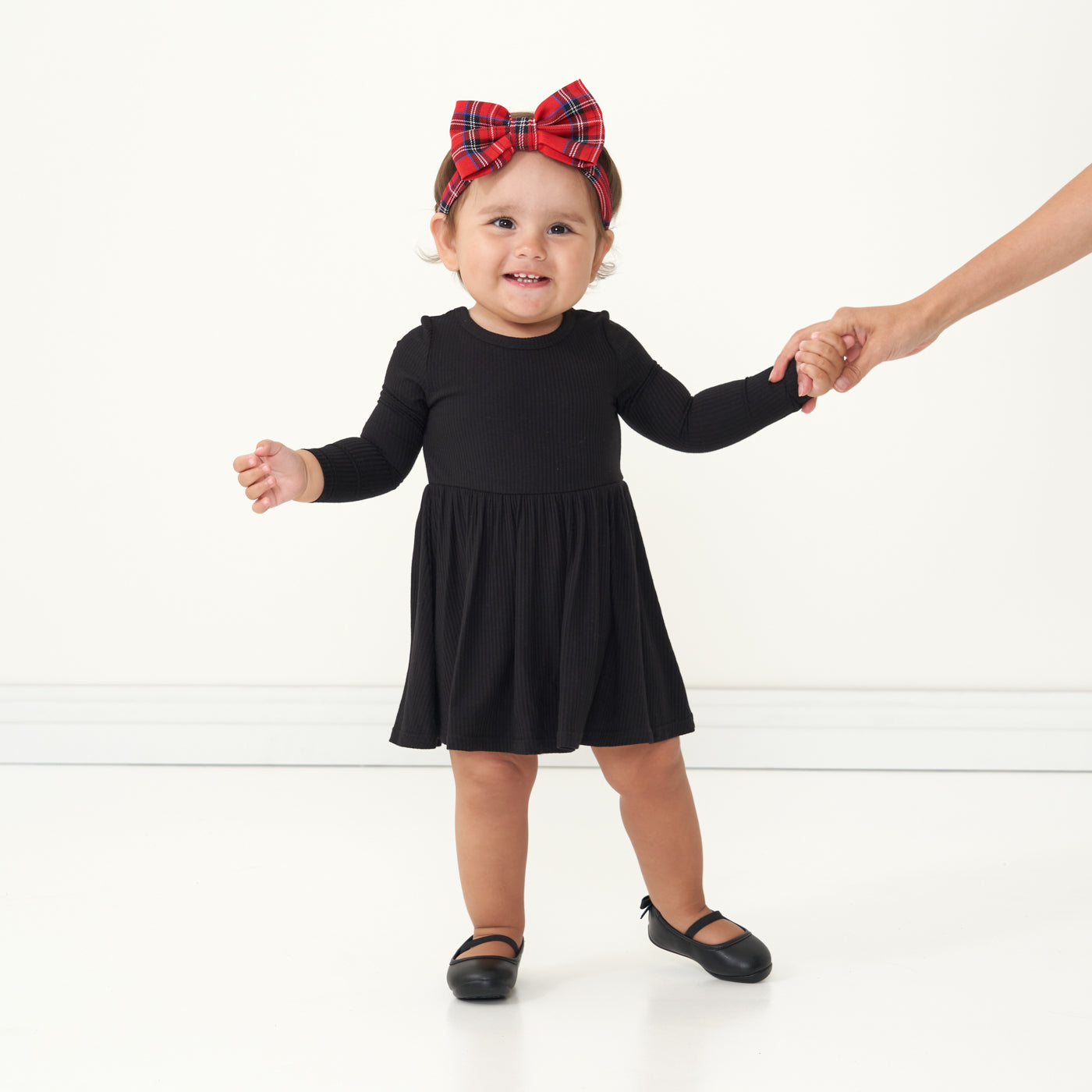 Child wearing a Black ribbed twirl dress with bodysuit and coordinating Holiday Plaid luxe bow headband