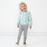 Child wearing a Unicorn Garden puff sleeve crewneck, matching luxe bow headband, and coordinating Heather Gray cozy leggings