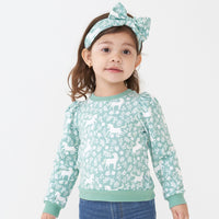 Close up image of a child wearing a Unicorn Garden puff sleeve crewneck and matching luxe bow headband