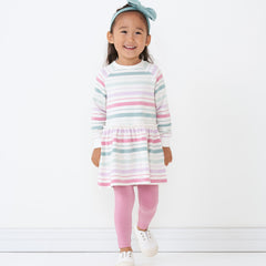 Child wearing Winter Stripes drop waist dress paired with Aqua Mist luxe bow headband and Garden Rose cozy leggings