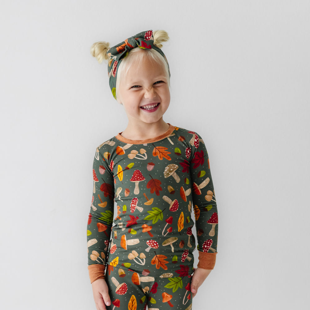 Child wearing a Woodland Forest two-piece pajama set and matching luxe bow headband