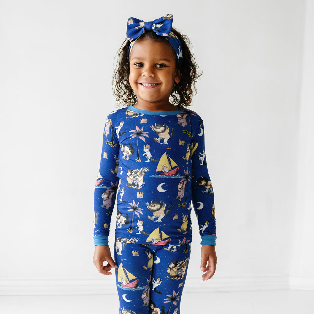Child wearing a Where the Wild Things Are two piece pajama set paired with a matching luxe bow headband