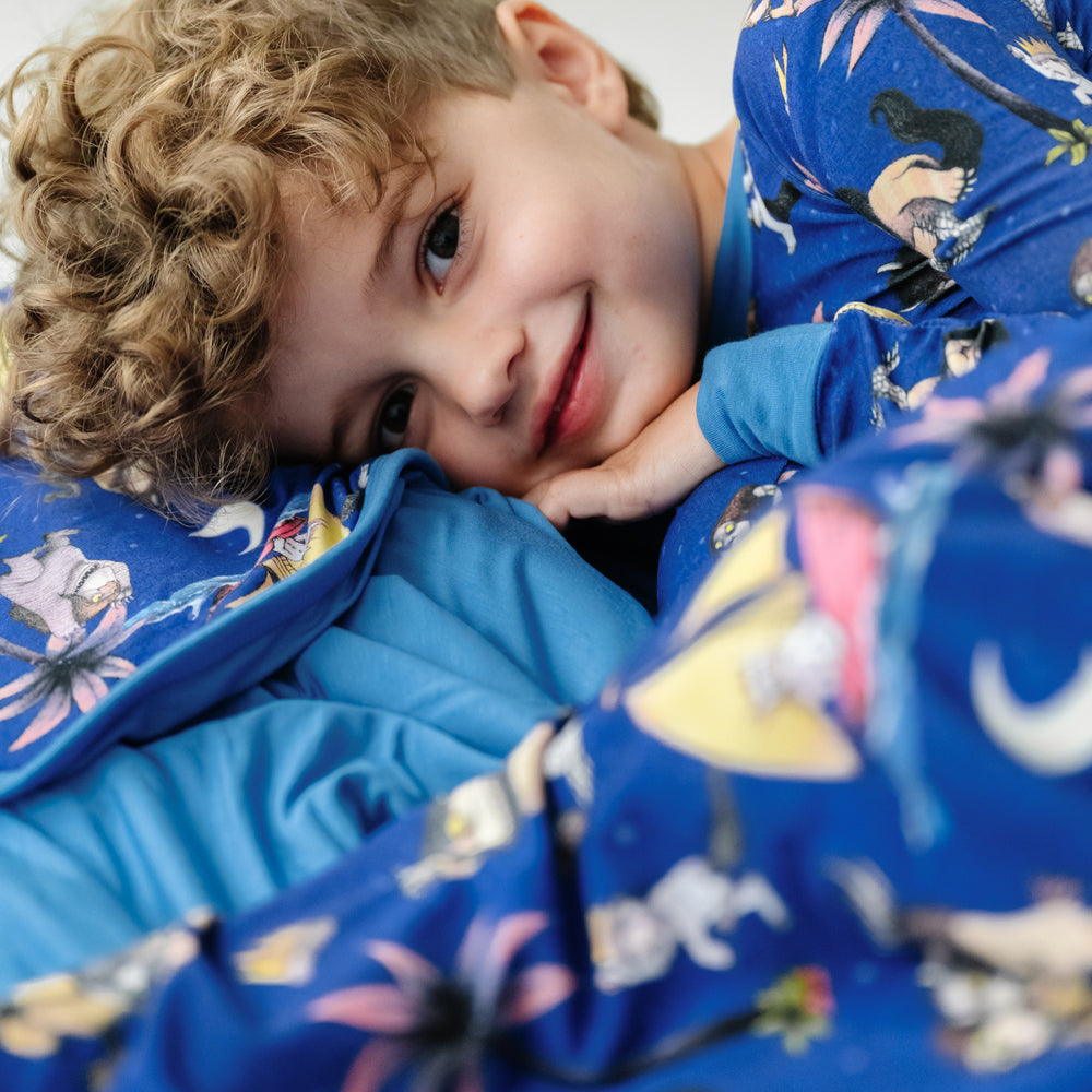 Close up image of a child laying on a Where the Wild Things Are cloud blanket and wearing a matching two piece pajama set