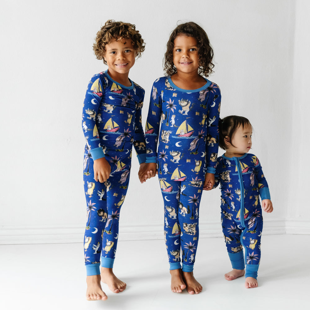 Three children holding hands playing wearing matching Where the Wild Things Are two piece pajama sets and a matching zippy