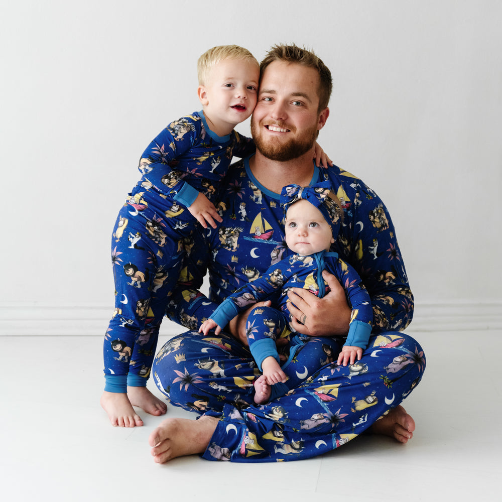 Father and his two children wearing matching pajamas. Dad is wearing men's Where the Wild Things Are men's pajama top and matching pants. Children are matching Where the Wild Things Are pajama sets and a matching luxe bow headband