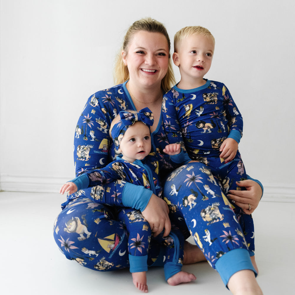 Mother and her two children wearing matching pajamas. Mom is wearing women's Where the Wild Things Are women's pajama top and matching pants. Children are matching Where the Wild Things Are two piece pajama sets and a matching luxe bow headband