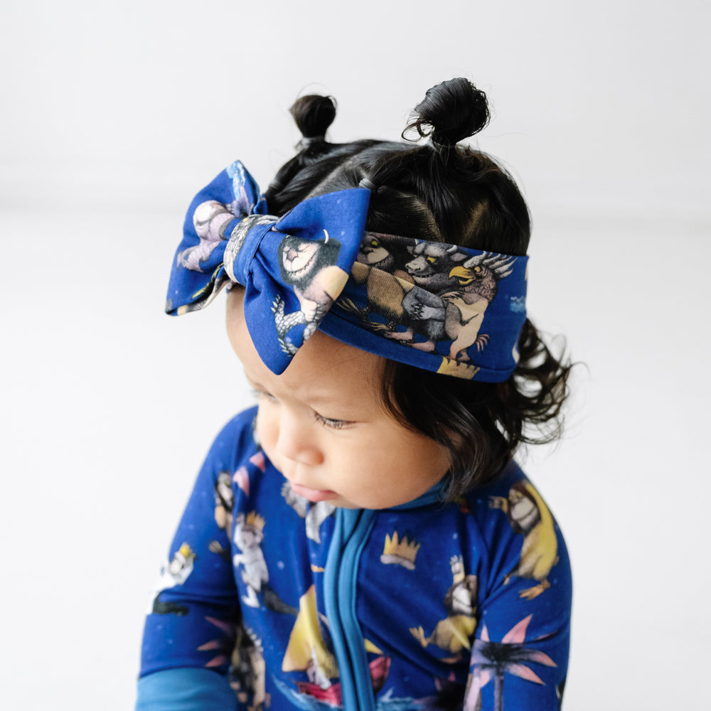 Close up image of a child wearing a Where The Wild Things Are luxe bow headband and matching zippy