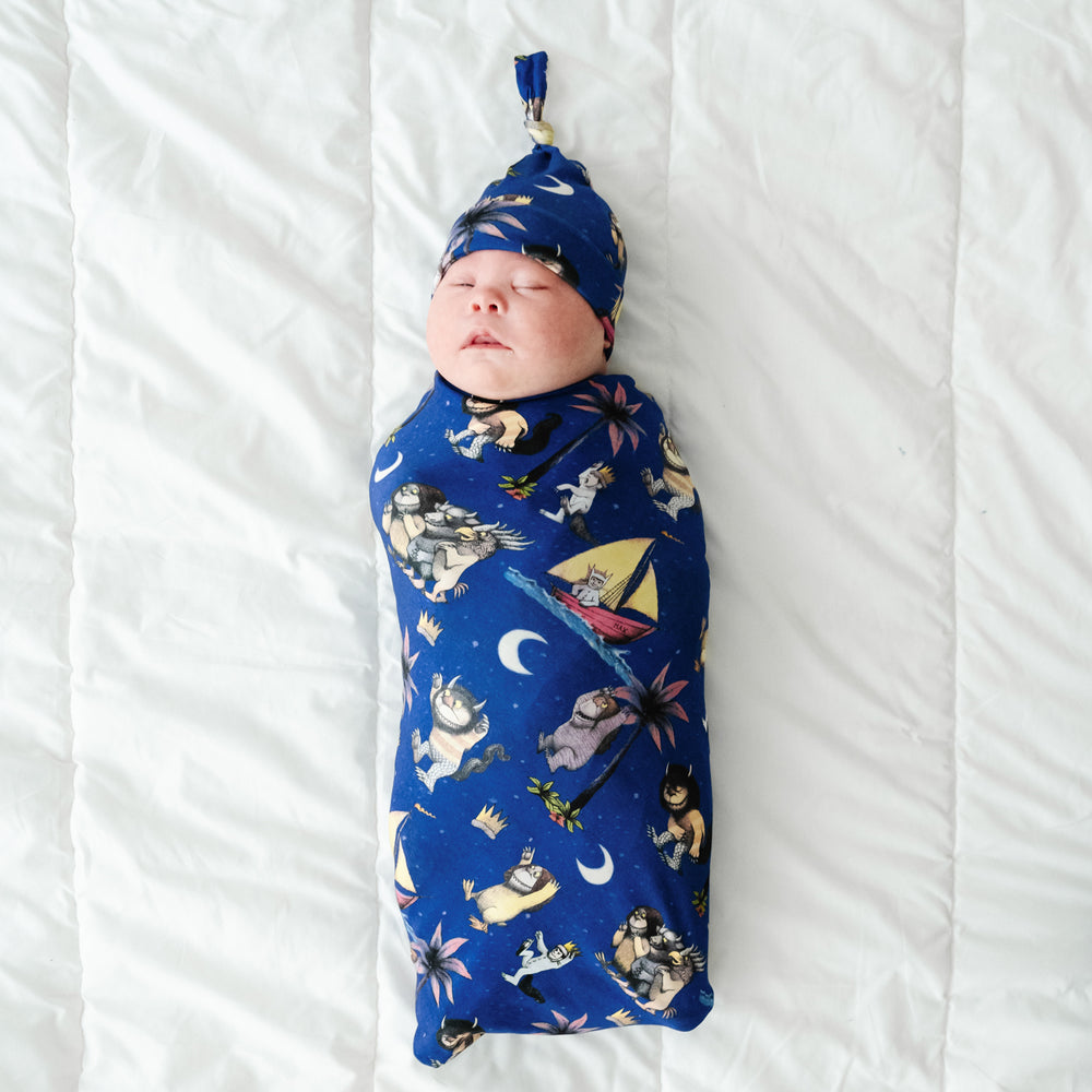 Child laying on a bed swaddled in a Where the Wild Things Are swaddle and hat set