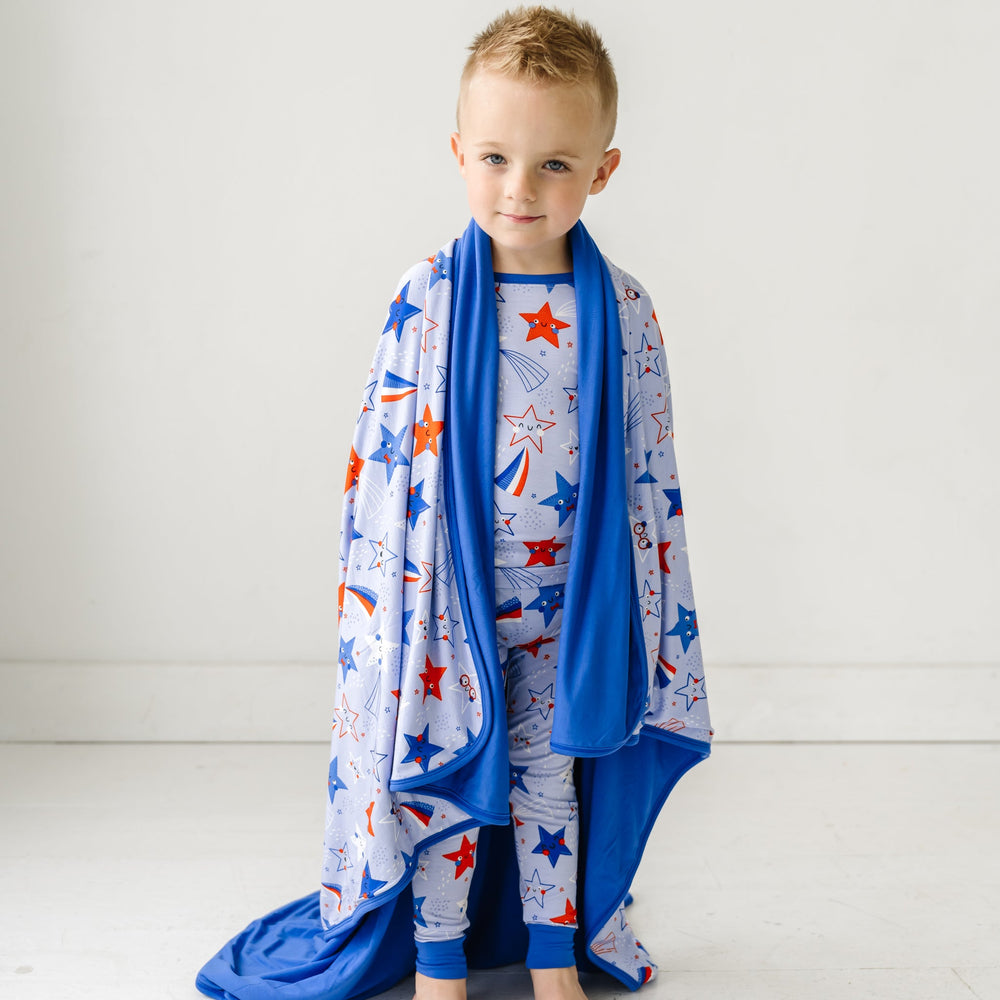 Child wearing a Blue Stars and Stripes Cloud Blanket on his shoulders that matches his Blue Stars and Stripes printed two piece pajama set