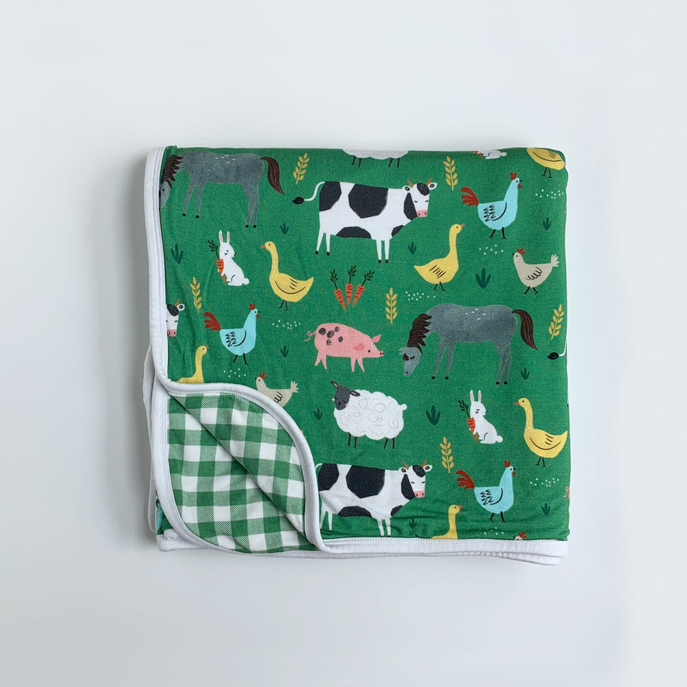 Click to see full screen - Flat lay image of tripe-layer large cloud blanket in green farm animals print. The blanket features a double-sided mix and match print, with one side showing the green farm animals and the other showing a white and green checkered print. The animals featu