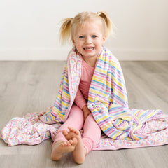 Double-sided rainbow and stripe printed blanket draped of child's shoulders