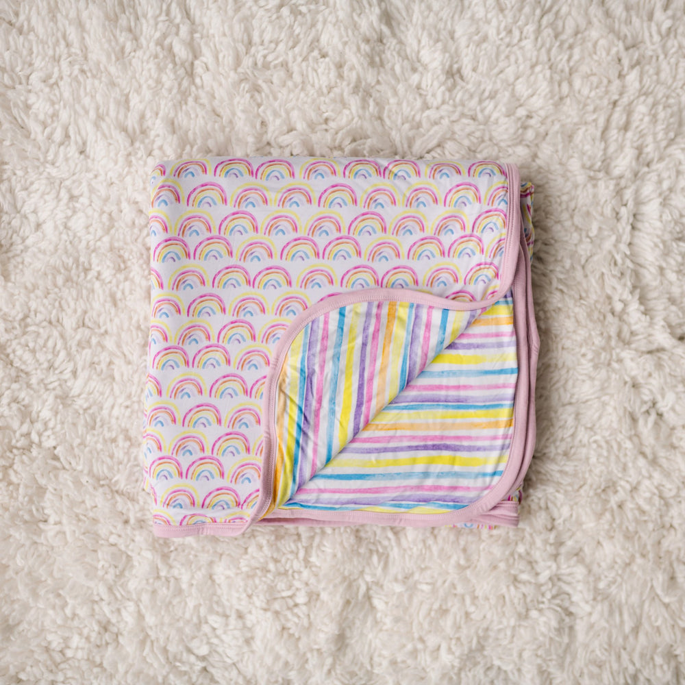 Image of double-sided rainbow and stripe printed blanket folded into a square