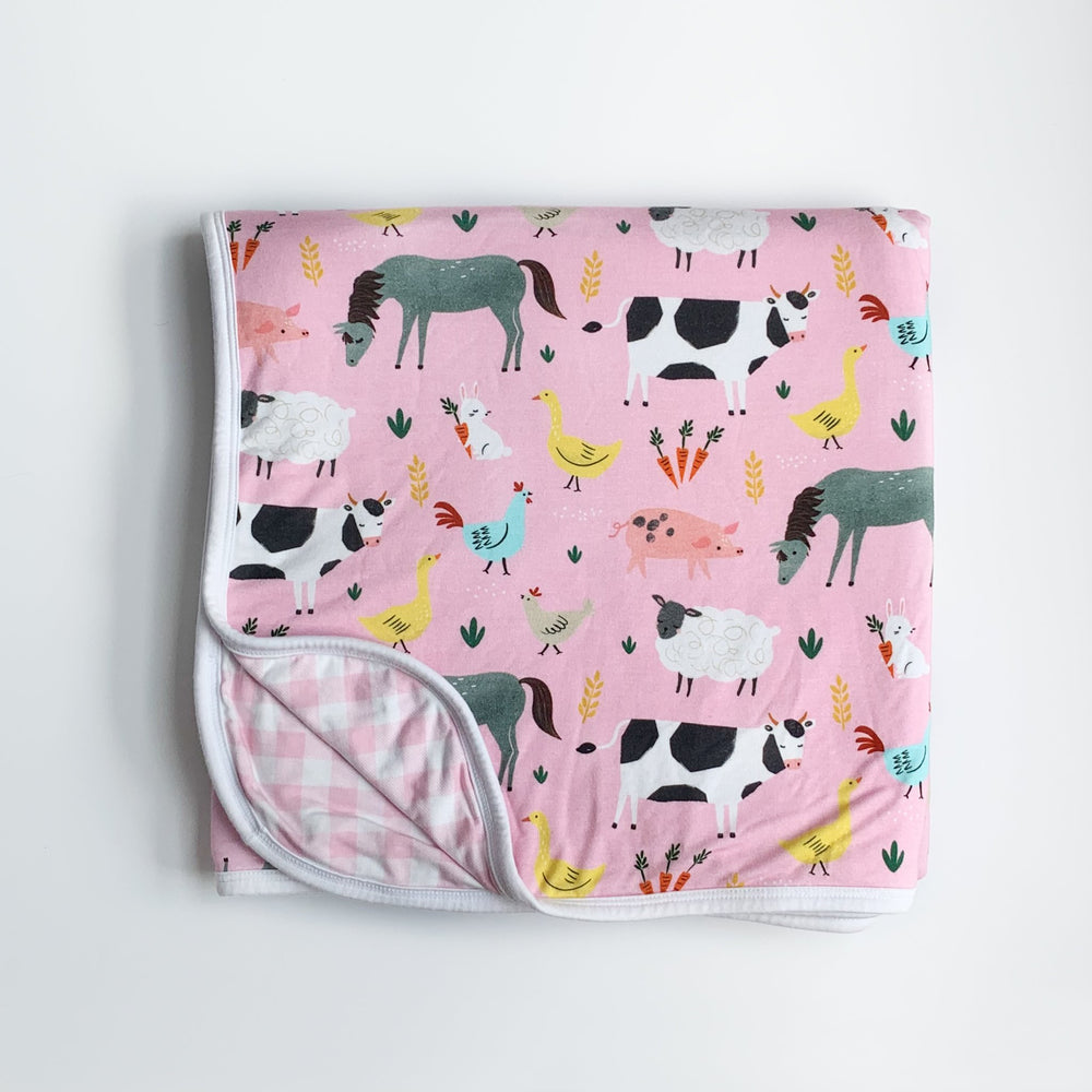 Flat lay image of Pink Farm Animals printed blanket with pink gingham backing