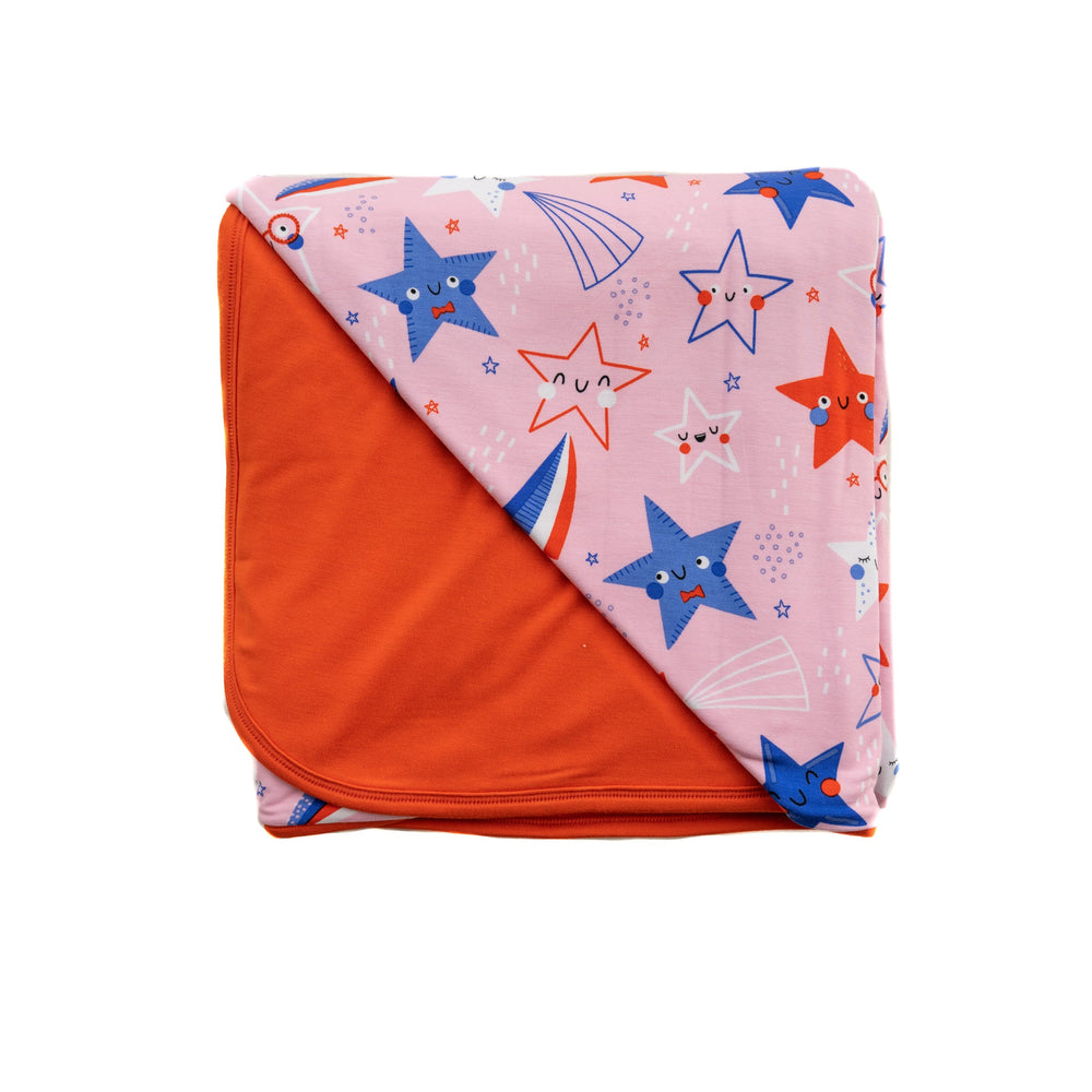 Flat lay image of a Pink Stars and Stripes printed cloud blanket showing off the solid red backing