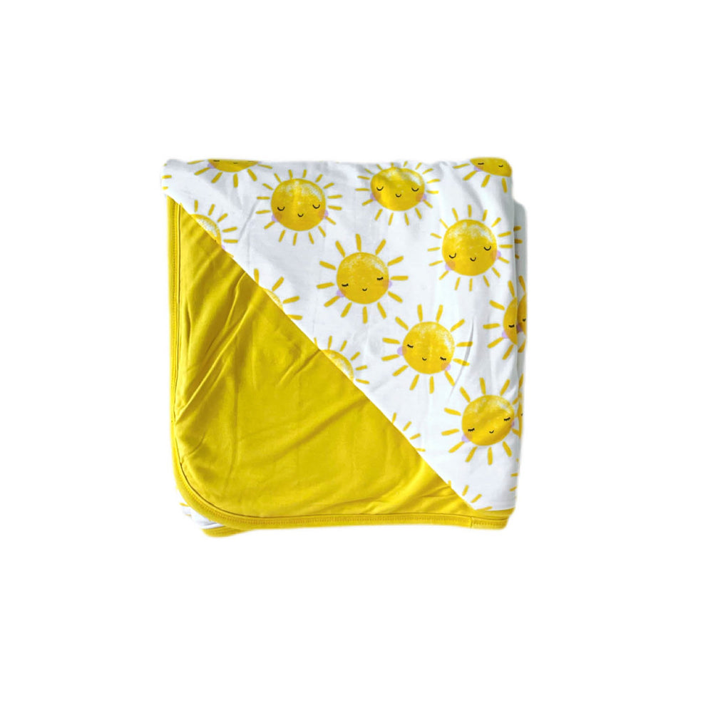Flat lay image of Sunshine printed triple-layer large cloud blanket. This blanket features our signature Sunshine print on one side, with a coordinating solid yellow on the other side. 