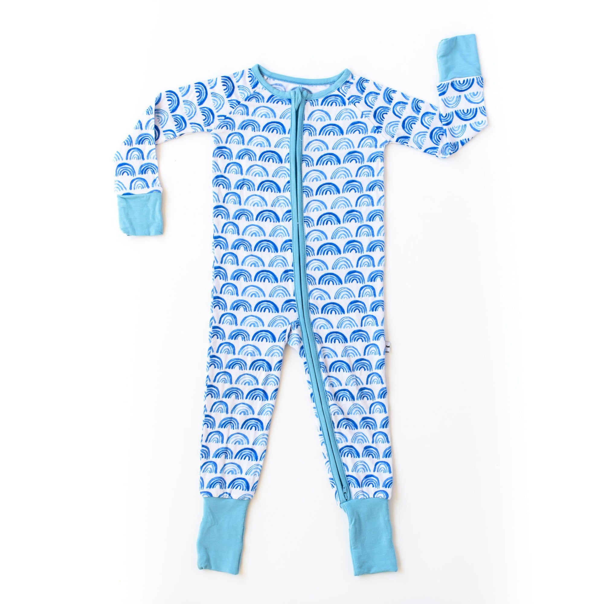 Flat lay photo of blue rainbow printed zip up romper. This print sits on a white background with shades of blue rainbows and sky blue trim details.