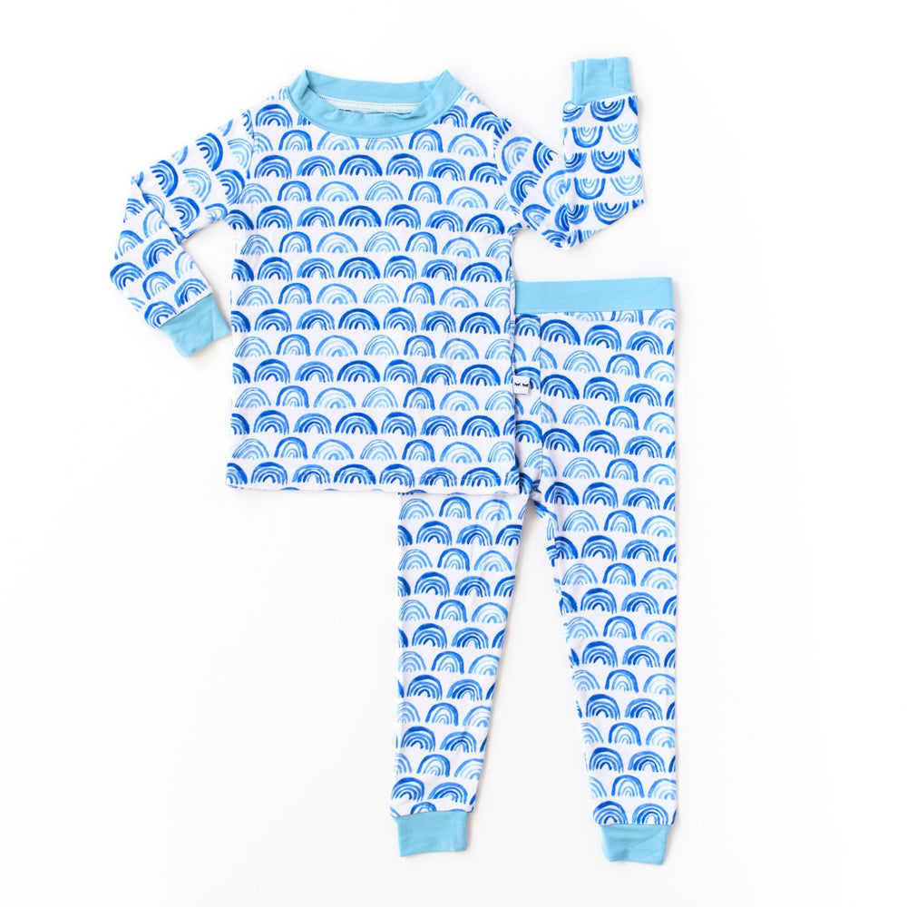 Flat lay photo of rainbow printed pajama set. This print sits on a white background with shades of blue rainbows and sky blue trim details.