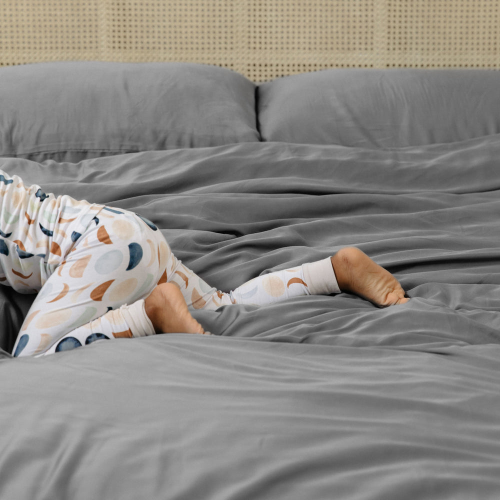 Close up of child wearing Luna Neutral pajamas crawling across the Bamboo Duvet Cover in Stone