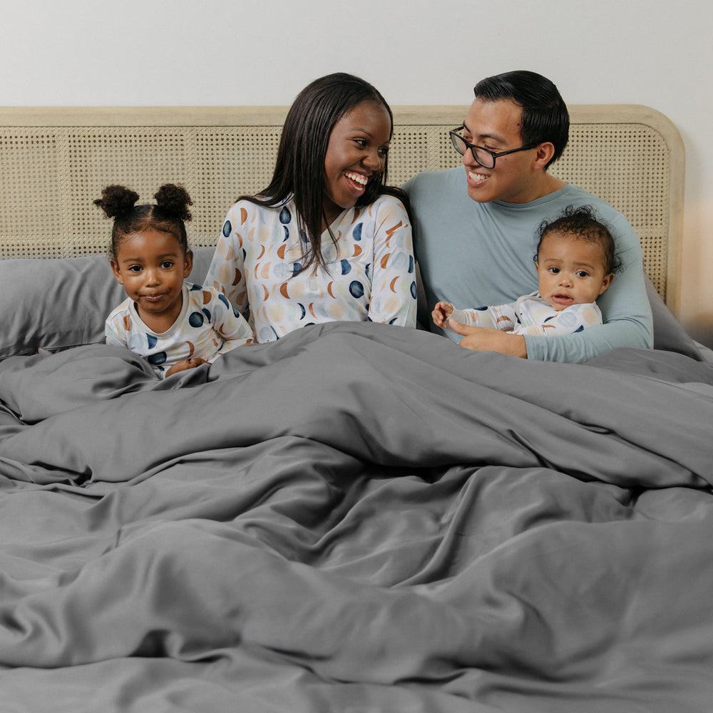 Family sitting up in bed wearing Luna Neutral pajamas tucked into their Bamboo Duvet Cover in Stone