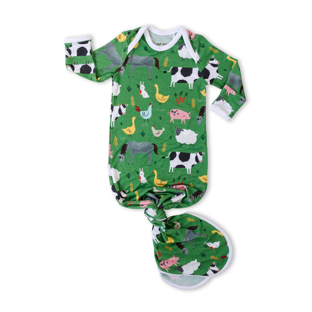 Flat lay image of infant knotted gown in green farm animals print. This print includes a green background with white trim details. The farm animals featured on this print include cows, pigs, ducks, sheep, pigs, chickens, and bunnies. 
