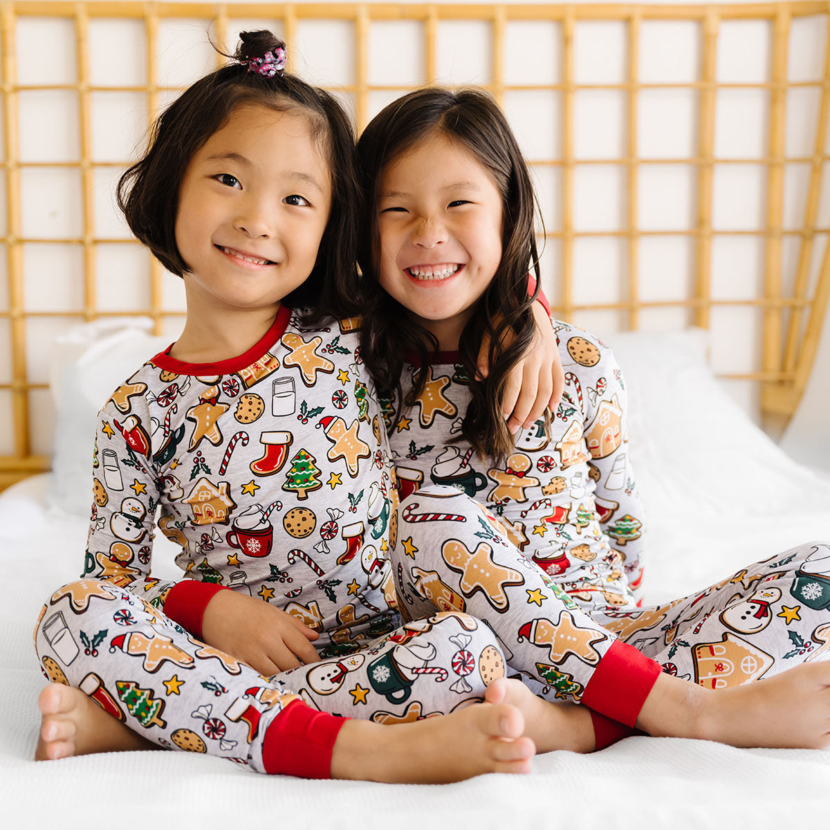 Two children sitting together on a bed wearing matching Holiday Treats two piece pajama sets