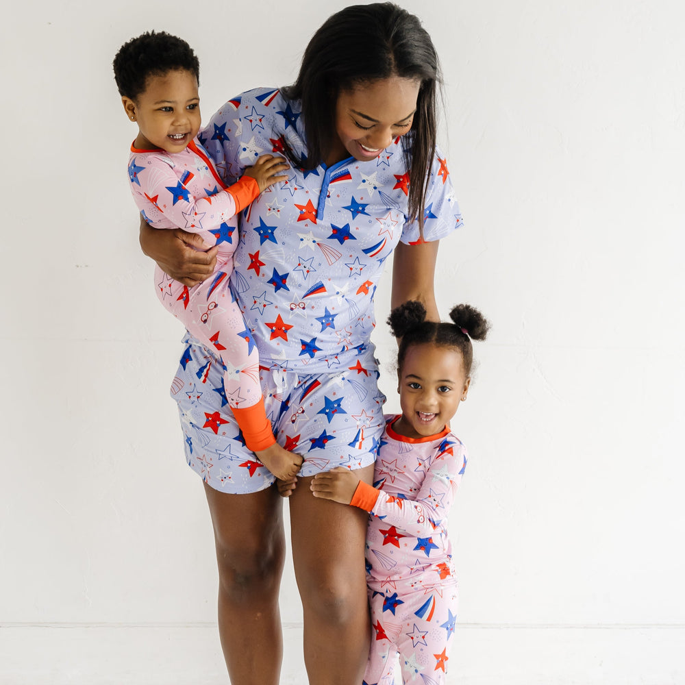 Woman with her two children. Mom is wearing Blue Stars and Stripes printed women's pajama shorts and matching women's pajama top. Children are coordinating in a Pink Stars and Stripes printed zippy and two piece pajama set