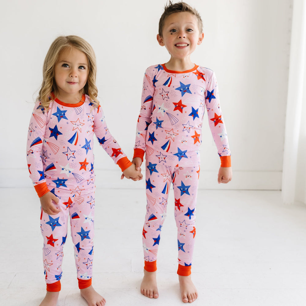Two children holding hands wearing matching Pink Stars and Stripes printed two piece pajama sets
