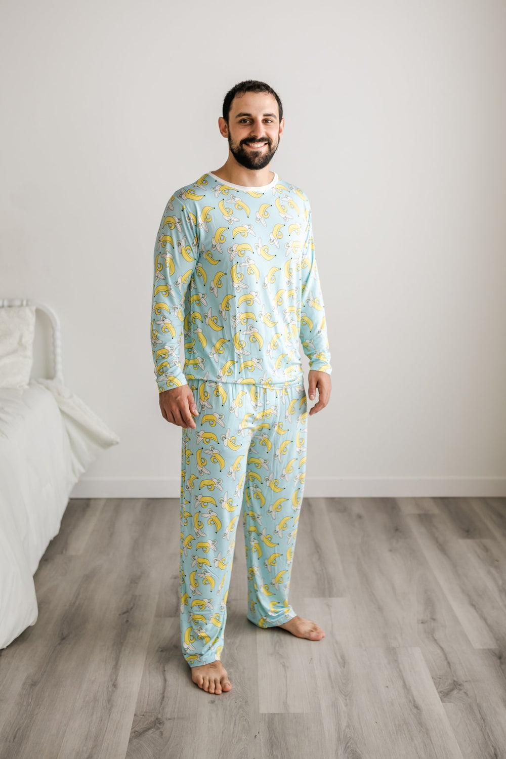 Click to see full screen - Male model wearing banana printed long sleeve pajama top with matching pajama pants. This print features a light blue background with pops of yellow coming from the bananas. The pajama top also features a white trim accent on the collar.