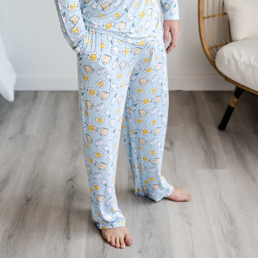 Image of male model wearing Blue Breakfast Buddies printed pajama pants. The pajama pants are featured having pockets. The breakfast foods featured on this print include sunny side up eggs, toast, and milk.