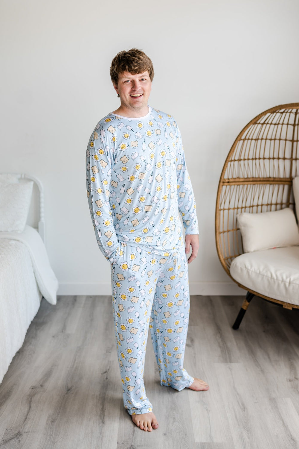 Image of male model wearing Blue Breakfast Buddies printed pajama pants with matching long sleeve pajama top. The breakfast foods featured on this print include sunny side up eggs, toast, and milk.