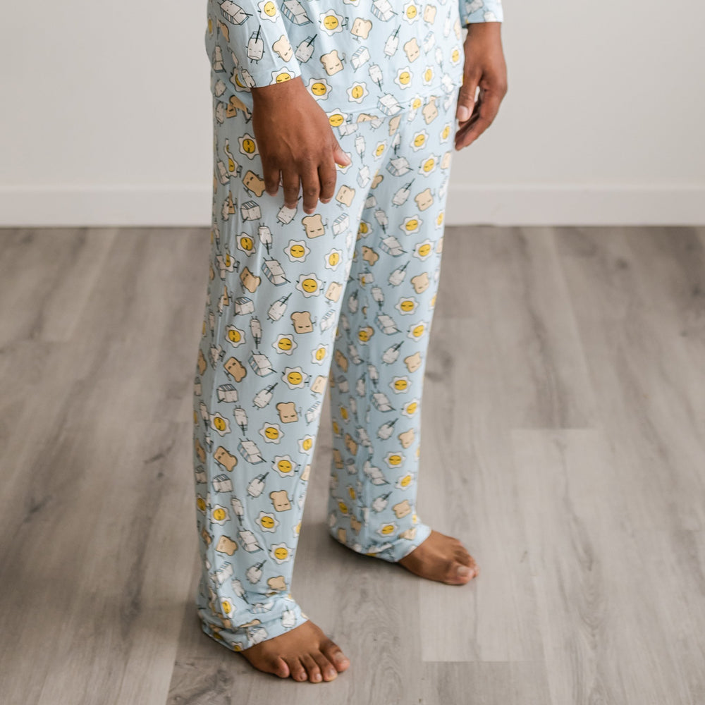 Image of male model wearing Blue Breakfast Buddies printed pajama pants. The breakfast foods featured on this print include sunny side up eggs, toast, and milk.