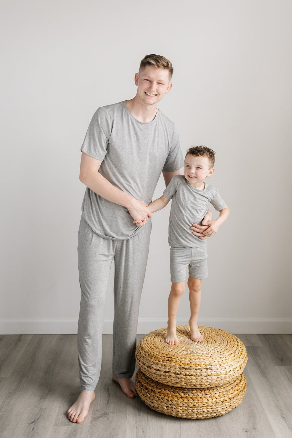Image of father and son wearing matching heather gray pajama sets. The dad is shown wearing a short sleeve pajama top and pajama pants, while the son is shown wearing a two-piece short sleeve and shorts pajama set. 